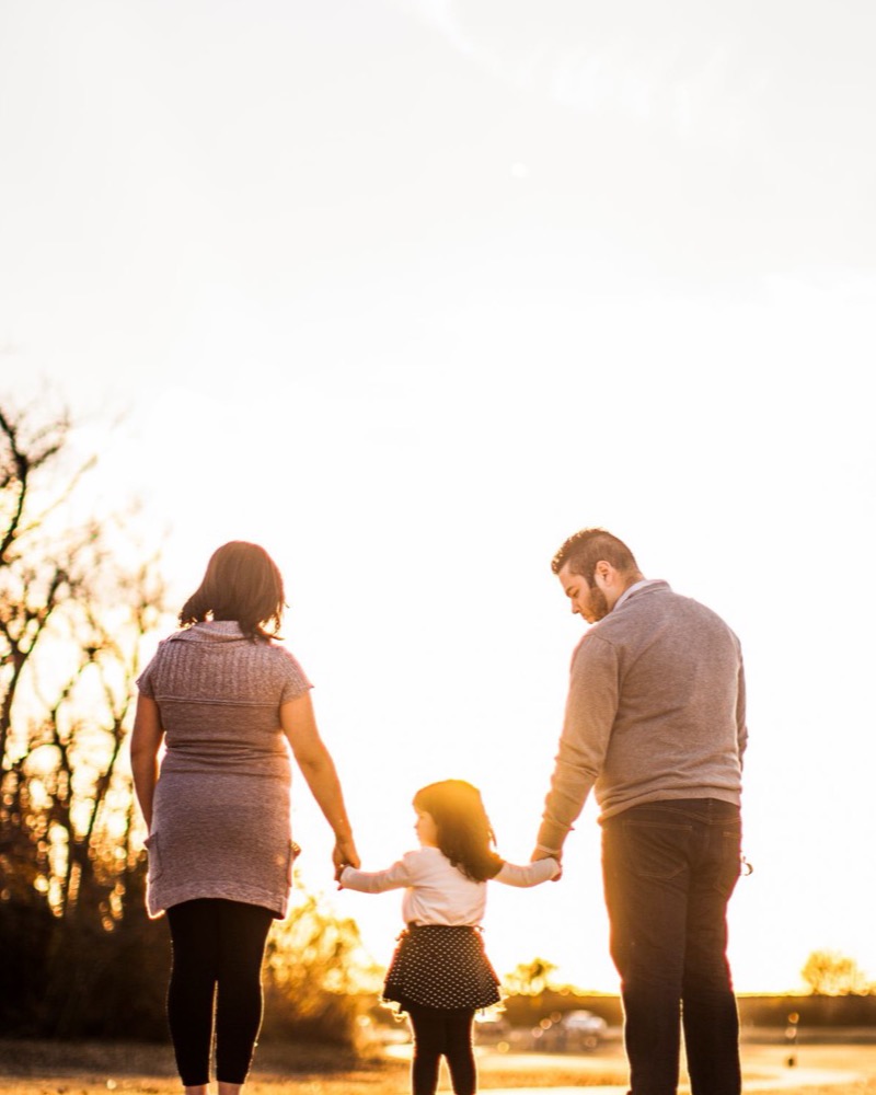 Familia vista de espaldas cogida de la mano caminando al aire libre durante la hora dorada, acompañamiento psicológico en diversidad funcional en Komit Psicología