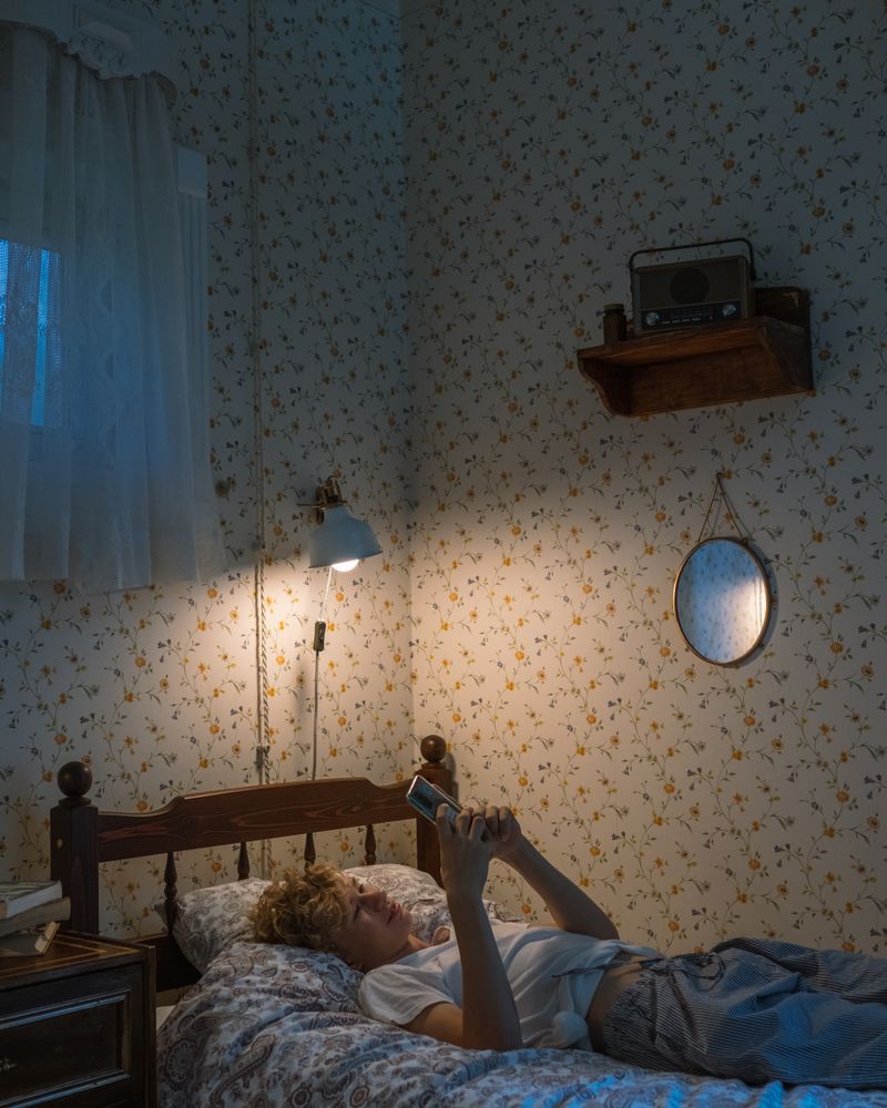 Adolescente tumbado en la cama por la noche mirando la pantalla del móvil con luz cálida de lámpara, terapia de la adicción a las pantallas en adolescentes en Komit Psicología