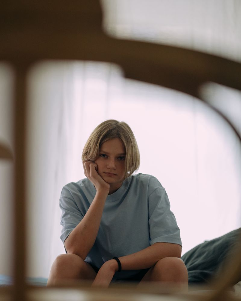 Adolescente pensativa con la mano en la mejilla junto a la ventana con luz natural cálida, terapia de la ansiedad en adolescentes en Komit Psicología