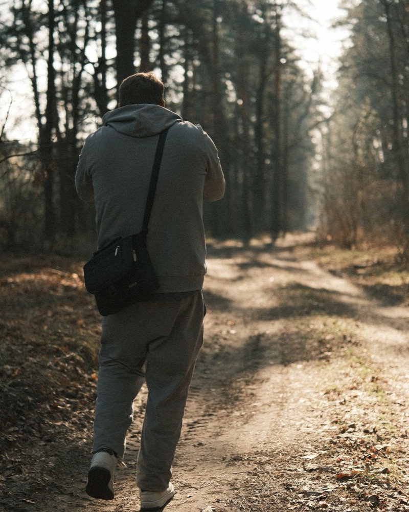 Hombre visto de espaldas caminando solo por un camino de tierra en un bosque otoñal iluminado por luz cálida, tratamiento del trauma en adultos en Komit Psicología