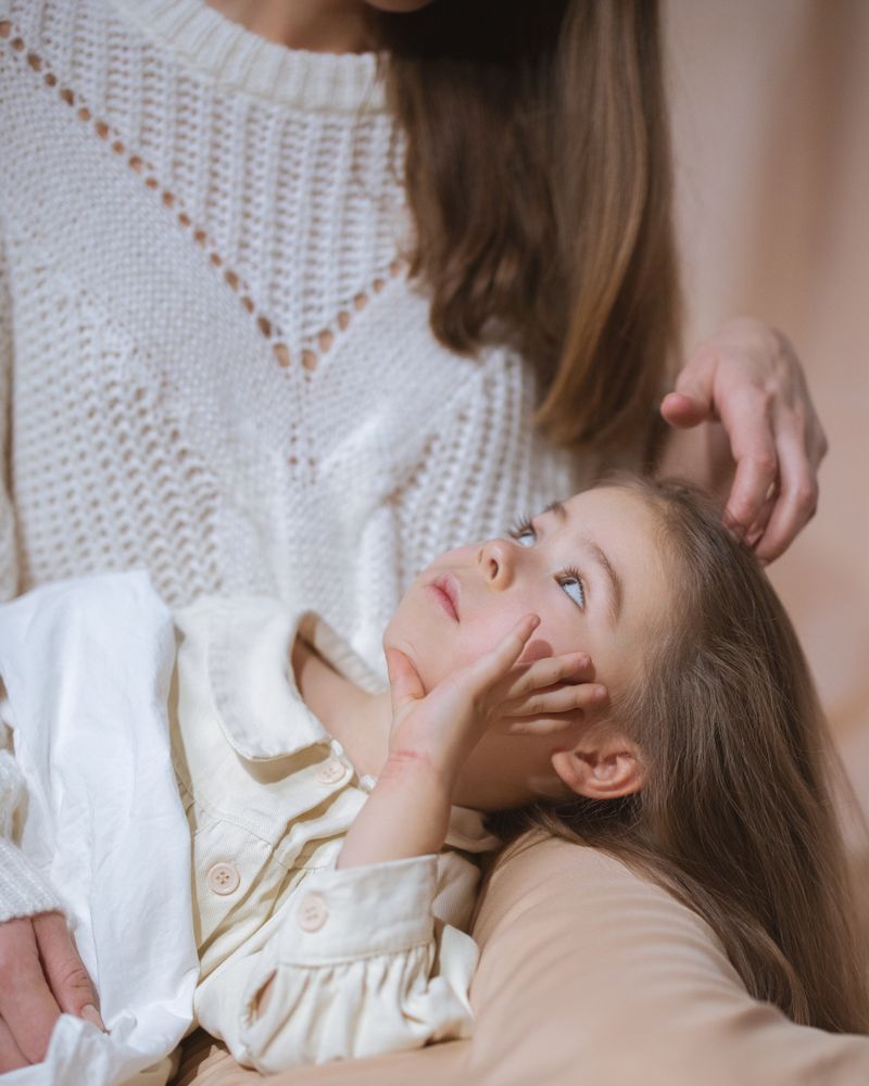 Niña recostada con calma en el regazo de su madre, que la acaricia con ternura bajo una luz cálida y suave, terapia de la depresión infantil en Komit Psicología