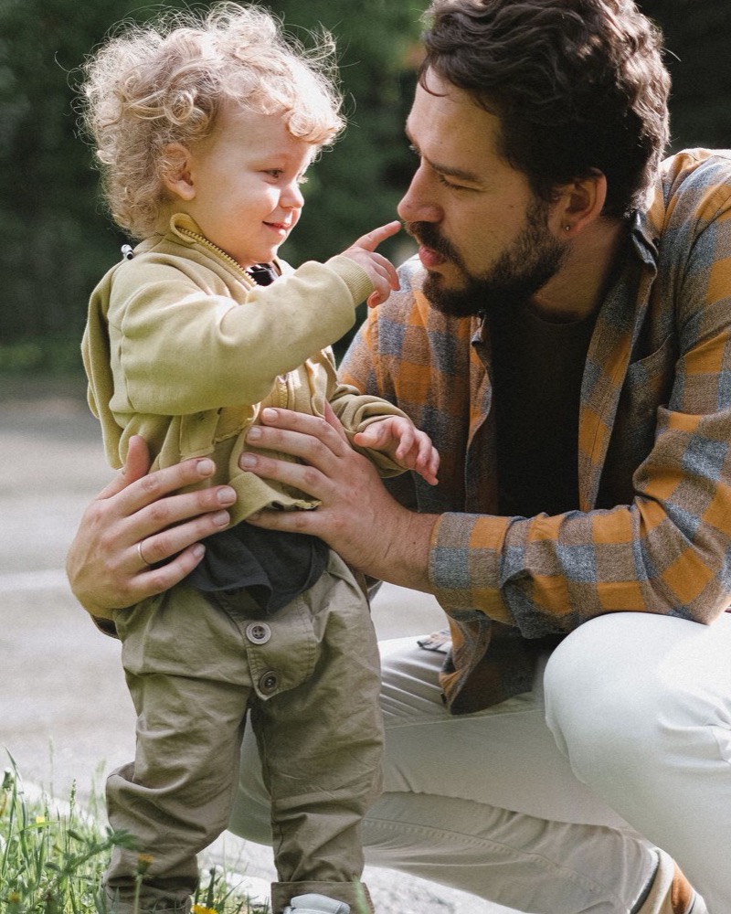 Padre agachado a la altura de los ojos de su hijo pequeño, sonriendo con calma mientras el niño le toca la cara con curiosidad al aire libre con luz natural cálida, intervención en problemas de conducta infantil en Komit Psicología