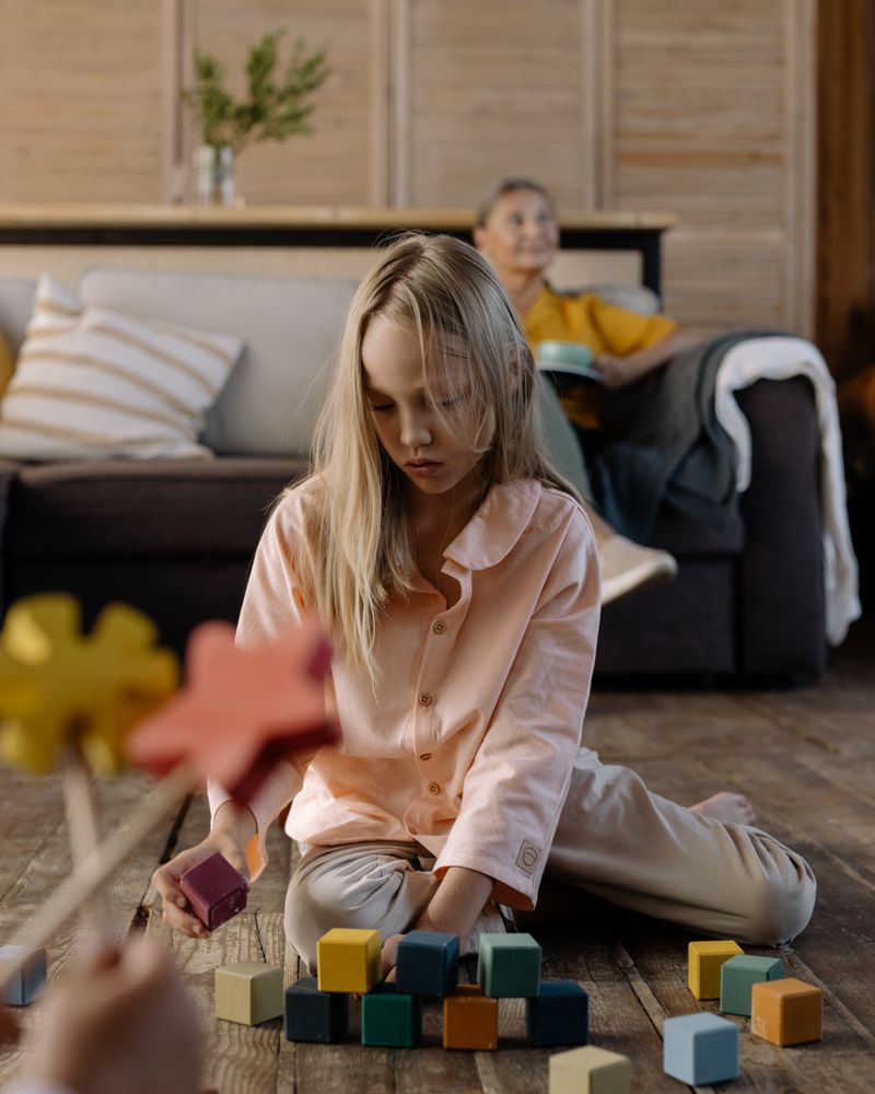 Niña concentrada jugando con bloques de madera de colores sobre el suelo con luz natural cálida, terapia del TDAH infantil en Komit Psicología